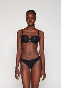 Conjunto de bikini preto com soutien estruturado e acolchoado, tiras finas e detalhe recortado; cuecas de cintura baixa a combinar com um discreto laço decorativo.