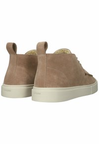 Zapatos de ante marrón hasta el tobillo con suela de goma blanca, con punta redonda, dos acentos en forma de lazo y un forro interior suave.