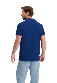 Marineblauw polo-shirt met korte mouwen en een kraag, van de achterkant weergegeven, met een zoomlabel en een gladde textuur.