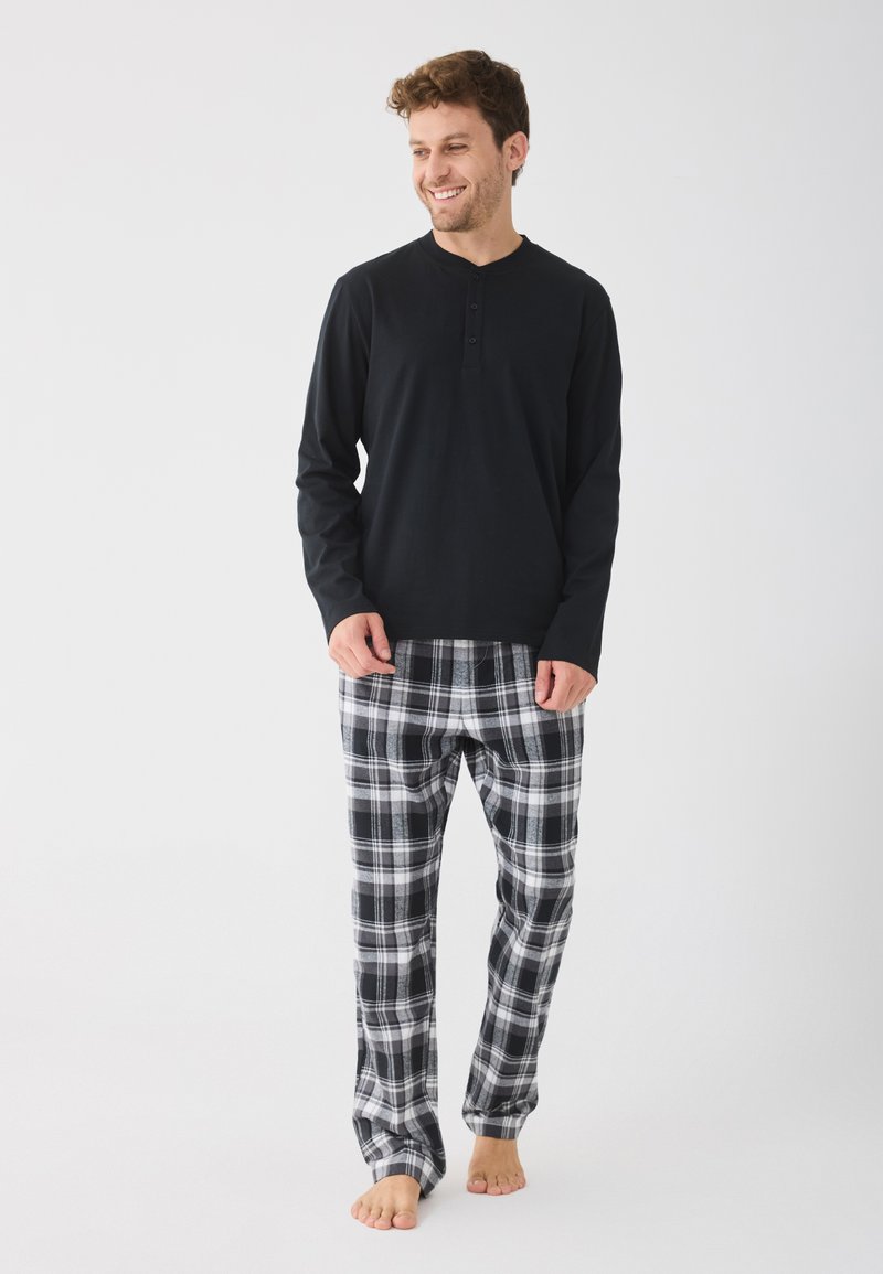 Haut henley à manches longues noir avec trois boutons, associé à un pantalon de pyjama à carreaux noir et blanc, offrant une coupe douce et décontractée.