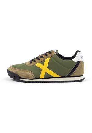Green sneaker with yellow X design, suede and canvas material, black laces, rubber sole, and white heel accent.