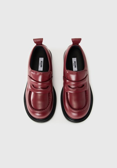 Pár tmavočervených kožených mokasín s čiernymi podrážkami a pútkami, so širokými pásmi cez vrch a označenými stielkami.