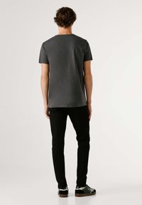 Kratka siva majica z okroglim izrezom, kombinirana s črnimi hlačami ohlapnega kroja in črnimi supergami z belimi poudarki.