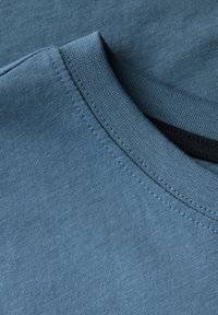 Blauwe katoenen t-shirt stof met een ronde hals en zichtbare stiksels. De textuur is soepel, met een lichte glans en een gelijkmatige kleurverdeling.