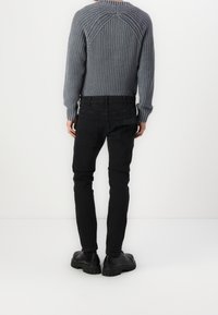 Šedý pletený svetr s texturou a kulatým výstřihem, v kombinaci s černými slim-fit džíny a masivními černými botami, pohled zezadu.