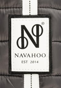 Étiquette noir et blanc avec le texte "NAVAHOO EST 2014" et un logo stylisé. Attacheé à un tissu matelassé gris avec une étiquette à rayures blanches.