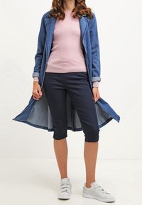 Abrigo largo de denim con exterior azul y forro azul claro, suéter de punto rosa, pantalones capri azul oscuro y zapatillas blancas, vista frontal.