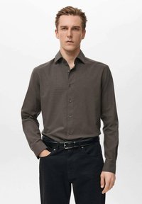 Camisa marrón de manga larga con un patrón texturizado, cuello abotonado, botones delanteros, combinada con pantalones negros y un cinturón negro.