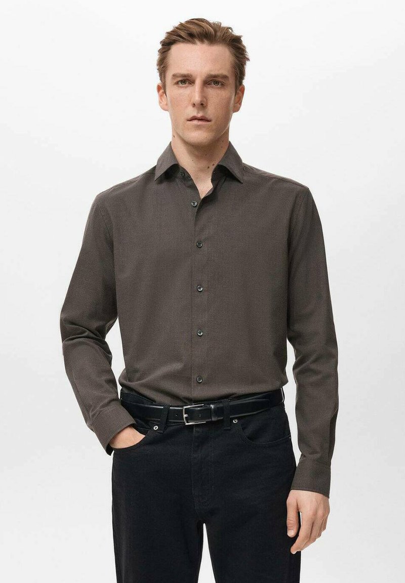 Camisa marrón de manga larga con un patrón texturizado, cuello abotonado, botones delanteros, combinada con pantalones negros y un cinturón negro.