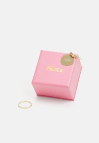 Auksu padengtas žiedas šalia rožinio kartono dėžutės, ant kurios įspausta "fine PIECES" ir apvali etiketė su užrašu "18K GOLD PLATED".