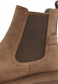 Stivaletto in camoscio marrone con pannello elastico laterale, dettagli cuciti, texture liscia e suola in gomma piatta. Nessun hardware o motivo prominente.