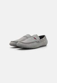 Mocassins en daim gris au design simple, avec un bord cousu et un petit logo coloré sur le côté. Texture douce et semelle flexible.