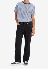 Randig blå och vit T-shirt med korta ärmar och blå krage, tillsammans med svarta jeans med raka ben och blå sneakers med vita detaljer.