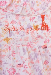 Tessuto a fiori nei toni del rosa, viola e giallo; presenta un colletto arricciato e la scritta ricamata "Sophie la girafe" con un motivo di giraffa.