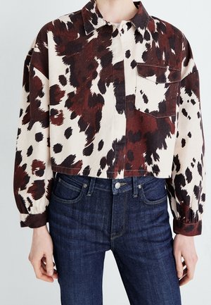 Kort skjorte med knapper med brunt og sort abstrakt dyreprint, enkelt brystlomme, kombineret med mørkeblå jeans.