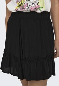 Falda negra de longitud a la rodilla, hecha de una tela suave, con un dobladillo con volantes y una cinturilla elástica para mayor comodidad y facilidad de uso.