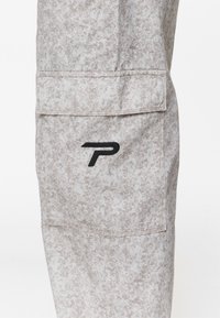 Lichtgrijze textuurbroekzak met klep en zwart gestileerd "P"-logo geborduurd op de voorkant van de zak.