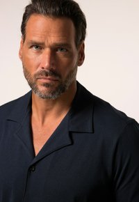 Mörkblå kortärmad skjorta med krage, med knappstängning och en jämn textur. Tyget verkar lätt och något figursytt.