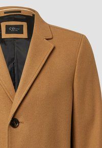 Bruine wolmix jas met gegoten revers, een zwarte voering en een enkele knoopsluiting. Soepele textuur met een getailleerde pasvorm.