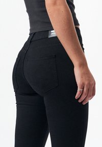 Vaqueros de mezclilla negra con un ajuste ceñido, que cuentan con una cinturilla estándar y dos bolsillos traseros. Textura mate con un detalle de costura mínimo.