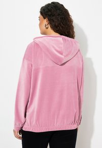Rosa Cordjacke mit Kapuze, die eine gerippte Textur, einen elastischen Saum und lange Ärmel aufweist, von hinten gezeigt.