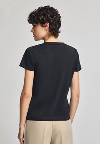 Svart kortärmad t-shirt i bomull med rund halsringning och en elegant, figurnära design. Ingen mönstring eller synliga detaljer.