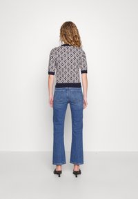 Marinblå och krämfärgad mönstrad stickad topp med korta ärmar, kombinerad med utsvängda blå jeans, sedd bakifrån.