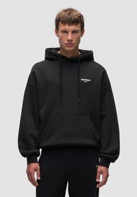 Sudadera con capucha negra, con un bolsillo frontal, puños acanalados y logo en el pecho. Tela gruesa y suave con un corte holgado.