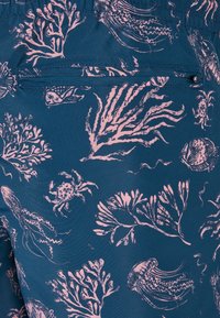 Bañadores de tela azul oscuro con un estampado de coral y vida marina en rosa claro. Incluyen un bolsillo trasero con cremallera para almacenamiento.