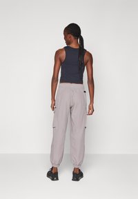 Top senza maniche nero abbinato a pantaloni cargo grigi chiari con orli elasticizzati e tasche laterali. Modello di spalle, indossa scarpe nere.