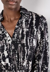Camisa de patrón en blanco y negro con cuello y detalles de botones, con un corte relajado y una textura de tela suave.