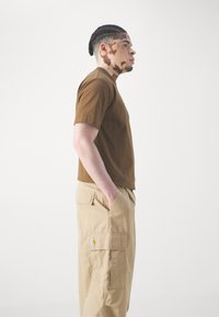 Brun kortærmet t-shirt parret med beige cargo bukser, der har et patch-logo, subtil tekstur og sidelommer.