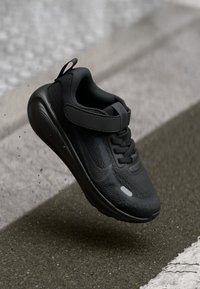 Schwarzer Sneaker mit einem strukturierten Mesh-Obermaterial, Klettverschluss und gepolsterter Sohle. Glatte Oberfläche mit dezentem Branding und ohne sichtbare Muster.