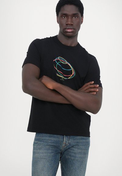 T-shirt en coton noir avec un graphique coloré de lignes entrelacées sur le devant. Associé à un jean en denim bleu.