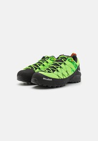 Chaussures de randonnée en mesh vert avec semelles en caoutchouc noir, dotées de lacets vibrants, d'un capuchon renforcé et d'un motif de grip texturé.