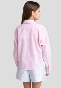 Camicia a righe rosa chiaro con colletto, maniche lunghe e polsini con bottoni. Il materiale sembra morbido, con una vestibilità rilassata e orlo curvo.