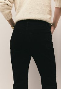 Sorte bukser med en tætsiddende pasform og baglommer, parret med en struktureret cremet sweater. Stoffet ser blødt og hyggeligt ud.