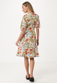 Blommig midiklänning med vit bakgrund och färgglada röda och blå blommor. Kort puffärmar och en utsvängd nederdel. Buren med svarta skor.