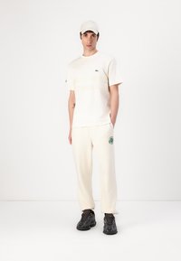 Lyscreme t-shirt med grønne vandrette striber og logo, parret med matchende sweatpants med grafisk accent i grøn, båret med sorte sneakers.