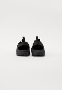 Czarne sneakersy z siateczkową cholewką, otwartym designem pięty i teksturowaną gumową podeszwą. Posiadają pętle ułatwiające zakładanie i smukły kształt.