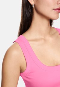 Pink sleeveless top with ribbed texture and wide neckline, paired with silver twist hoop earrings. Smooth skin tone visible.