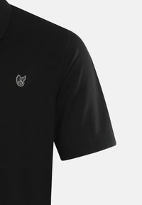 Musta polo-paita, jossa on lyhyet hihat, kauluskangas ja pieni brodeerattu logo rinnassa. Kangas vaikuttaa olevan teksturoitua.