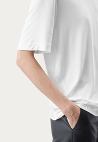 Hvid kort�ærmet t-shirt lavet af blød bomuld, med en afslappet pasform, glat tekstur og diskrete syninger, parret med sorte bukser.