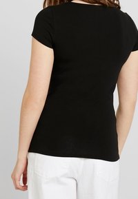 Camiseta negra de manga corta con cuello redondo, diseño ajustado, textura suave y detalles de costura visibles, combinada con pantalones blancos.
