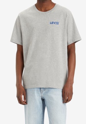 Grå bomuld T-shirt med korte ærmer, rund halsudskæring og en blå "LEVI'S"-logo på brystet. Båret med lyseblå denimjeans.