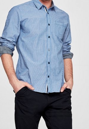 Camisa abotonada a rayas en azul claro y blanco. Cuenta con un solo bolsillo en el pecho, mangas largas enrolladas en los puños y botones oscuros.