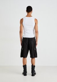 Pantaloni scurți negri cargo cu buzunare cu nasturi, împărțiți cu un top alb fără mâneci și cizme negre până la gleznă. Țesătura pare netedă și ușoară.