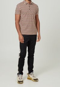 Polo à manches courtes avec un motif géométrique rouge et crème, associé à un pantalon noir avec une bande sur le côté, et des baskets légères.