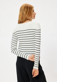 Gestreepte ribben top met lange mouwen in het wit met zwarte horizontale strepen, voorzien van een bootnek en een slim-fit silhouette.