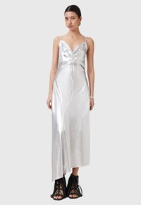 Abito slip in satin argentato con scollo a V profondo, dettagli arricciati sul busto, orlo asimmetrico e una texture liscia. Stivali alla caviglia neri con frange.